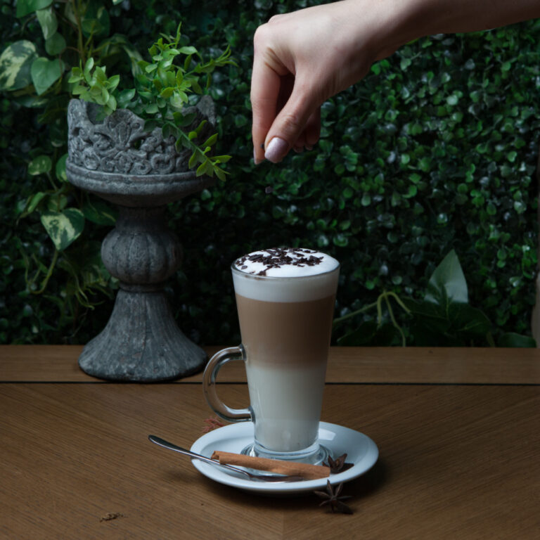 side-view-latte-with-cinnamon-chocolate-chips-human-hand-glass-cup